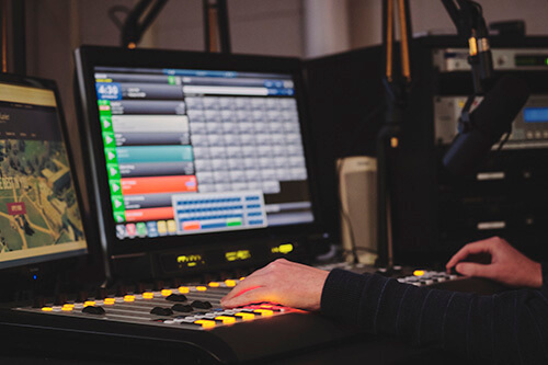 Person working at the radio station, on a computer and using a soundboard